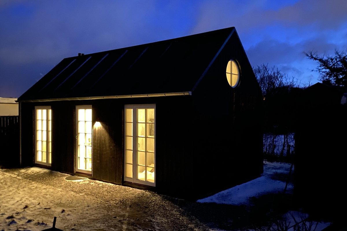 Sort sommerhus oplyst i aftenlys ved Skagen
