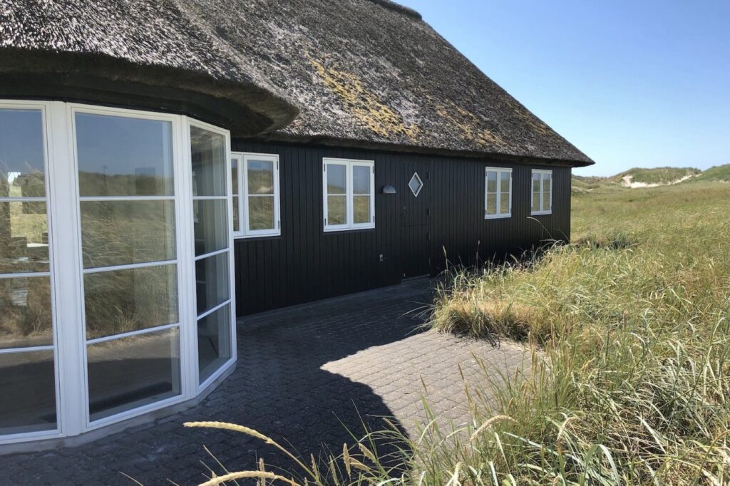 Sort sommerhus med stråtag og buet vinduesparti ved Skagen